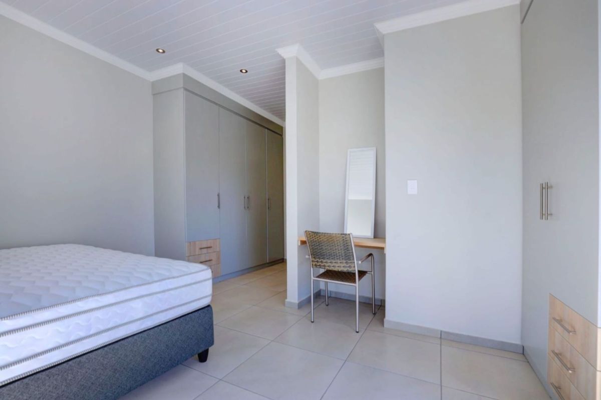 A bright bedroom featuring neutral tiled flooring, built-in cabinetry with integrated storage, and a dedicated vanity or desk nook.