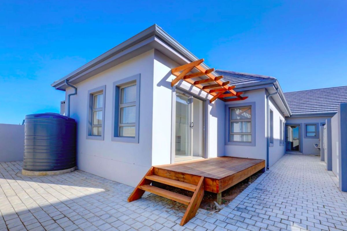 Rear exterior view featuring a timber deck, sliding glass doors, and a large water storage tank set on paved ground.
