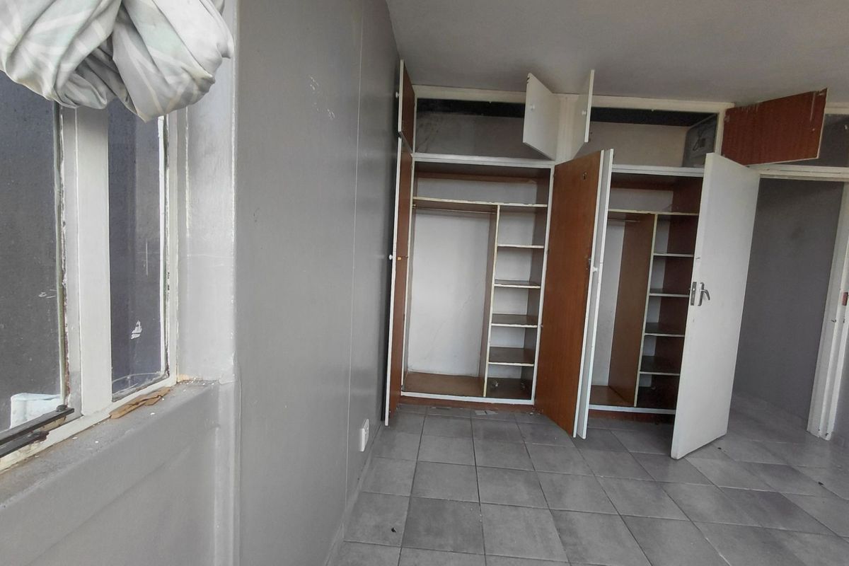 A vacant bedroom featuring built-in wooden cupboards with shelving and tiled flooring, offering a blank canvas for renovation.