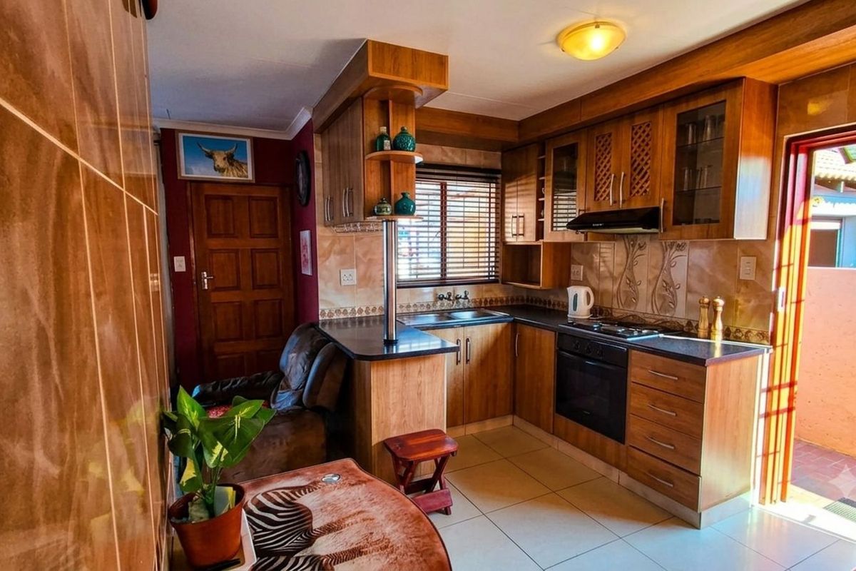 A functional kitchen featuring wood-finish cabinetry, built-in oven, hob, extractor fan, and tiled flooring with direct access to an outdoor area.