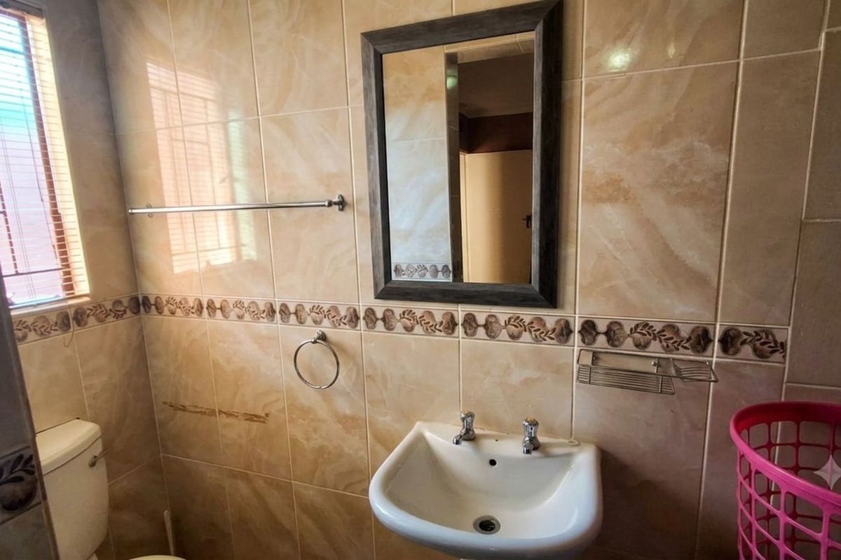 A functional bathroom featuring ceramic wall tiles, a pedestal basin, a toilet, and a wall-mounted mirror.