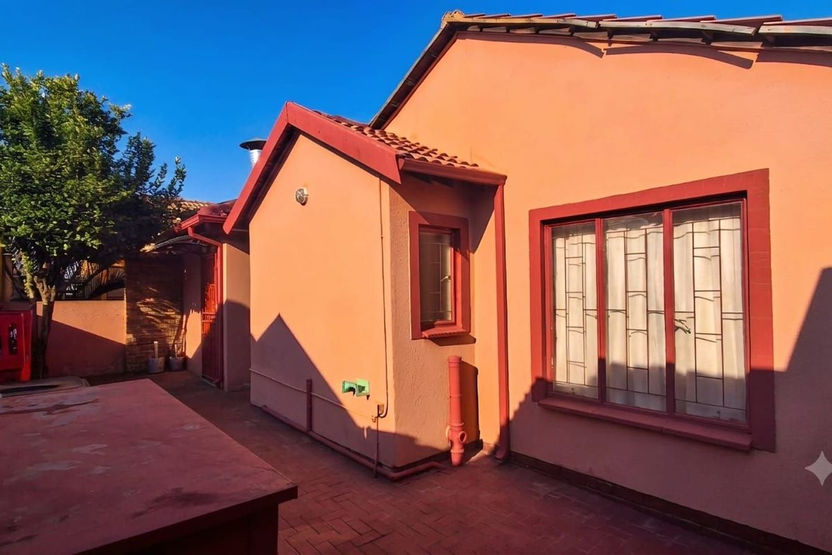 A view of the rear exterior of the house, featuring a paved courtyard area, terracotta-toned walls, and metal security window bars.