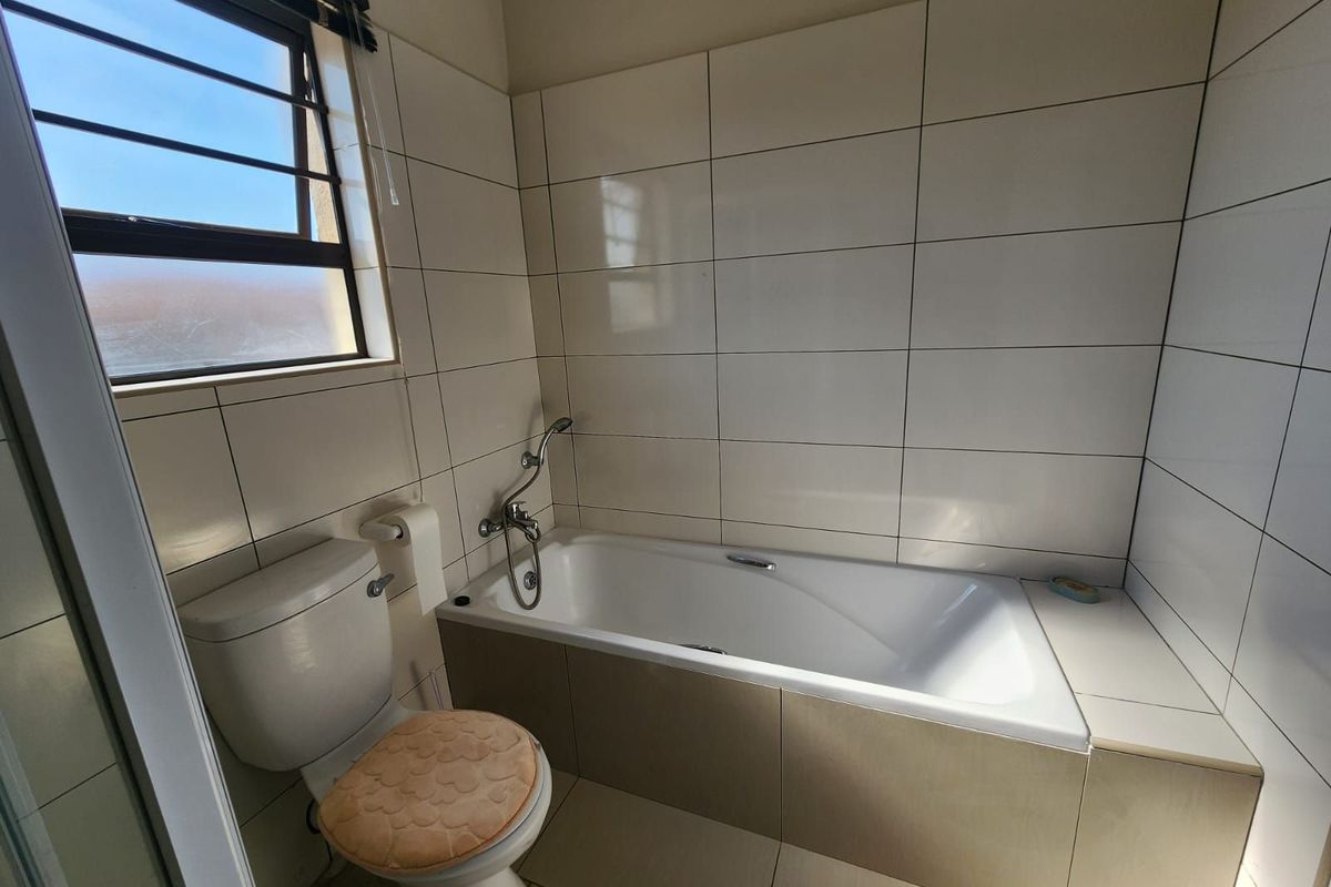 A functional bathroom featuring a built-in bathtub with shower mixer, tiled walls, and a standard toilet.