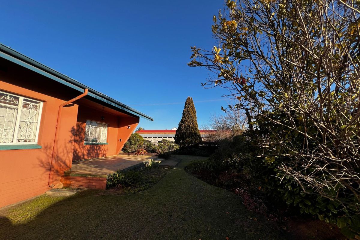 A view of the rear garden and patio area, featuring a paved walkway, established landscaping, and the side elevation of the house.