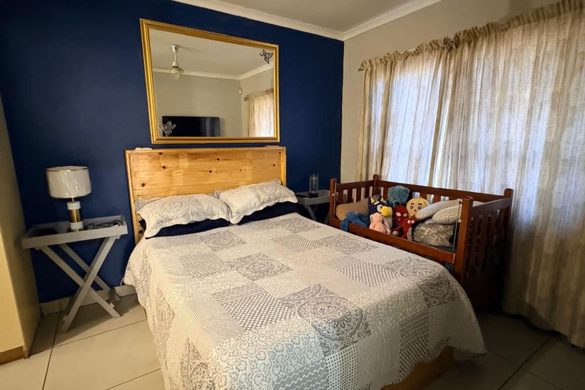 A bedroom featuring tiled flooring, a feature wall, and large windows with curtains, providing a functional and comfortable living space.