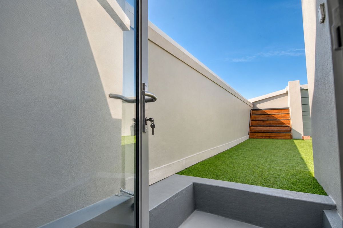 A view of a private rear courtyard featuring a low-maintenance artificial lawn, perimeter boundary wall, and a raised timber-clad planter box.