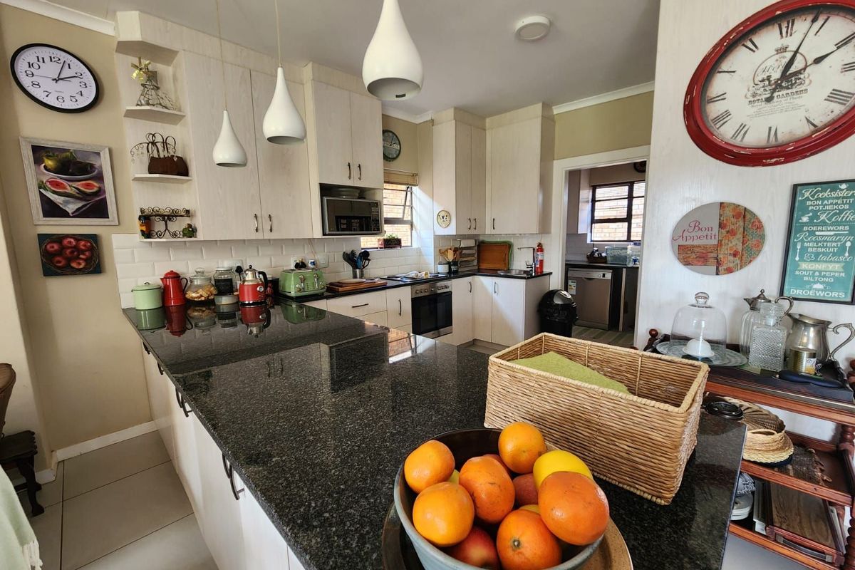 A well-maintained kitchen featuring granite countertops, subway tile backsplash, built-in appliances, and ample cabinetry, with an adjacent scullery area visible.