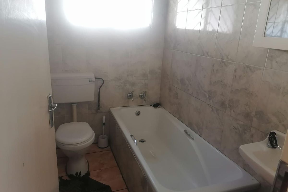 A functional bathroom featuring a standard bathtub, toilet, and wall-mounted basin with neutral wall tiling.