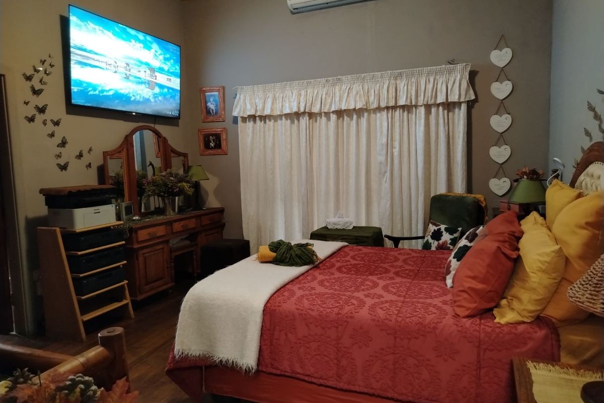 A cozy bedroom featuring a wall-mounted air conditioning unit, wooden flooring, and a large window dressed with curtains.