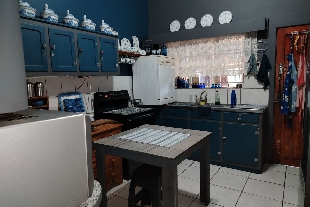 A functional kitchen featuring blue painted cabinetry, tiled splashbacks, a freestanding stove, and tiled flooring.