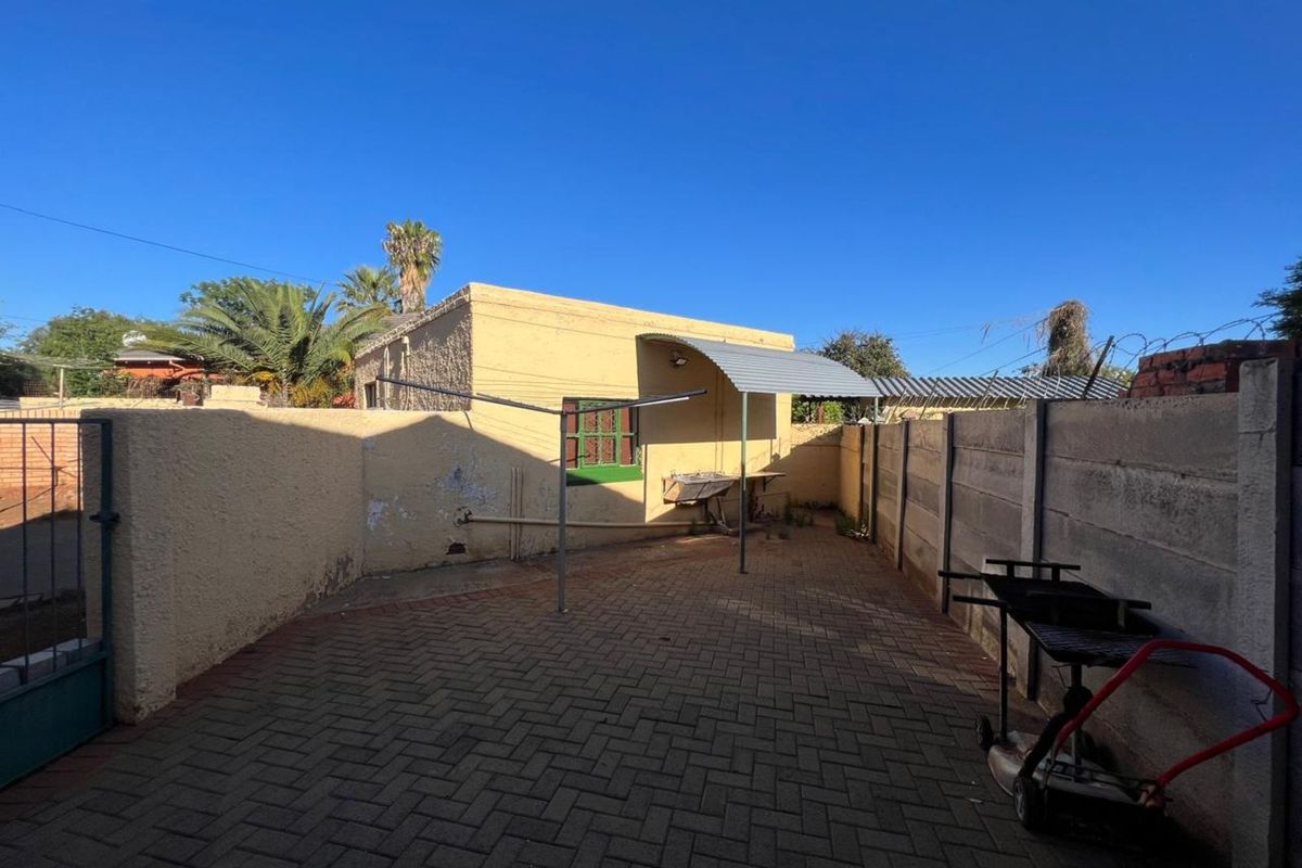 A paved rear courtyard area featuring a small covered patio section, perimeter boundary walls, and a metal washing line structure.
