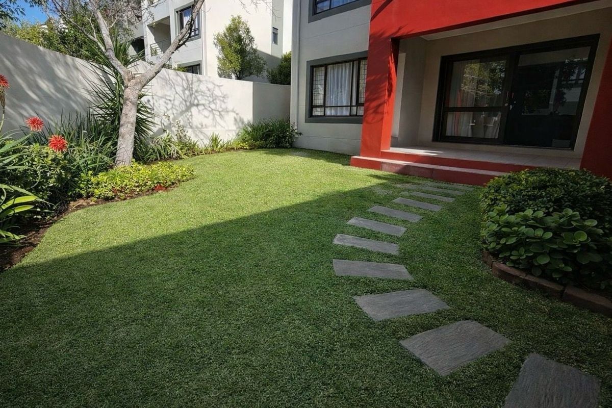 A well-maintained private garden featuring a manicured lawn, stone stepping path, and established landscaping, adjacent to the apartment's rear exterior facade.