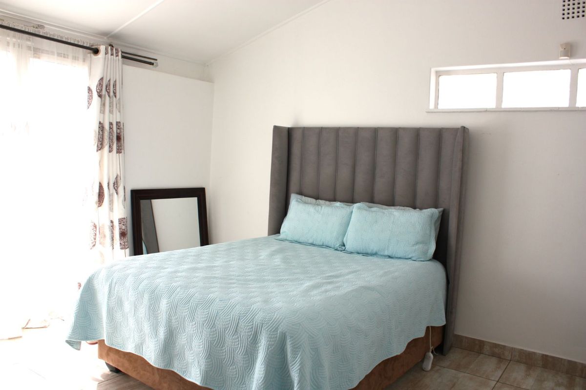 A bright bedroom featuring tiled flooring, a high-set horizontal window, and a glass sliding door providing natural light.