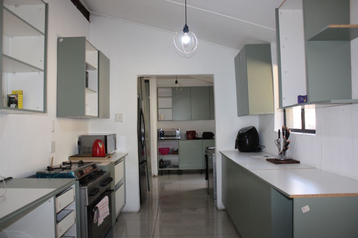 A functional kitchen featuring sage green cabinetry, tiled flooring, and a gas stove, with an adjoining scullery area for additional storage and prep space.