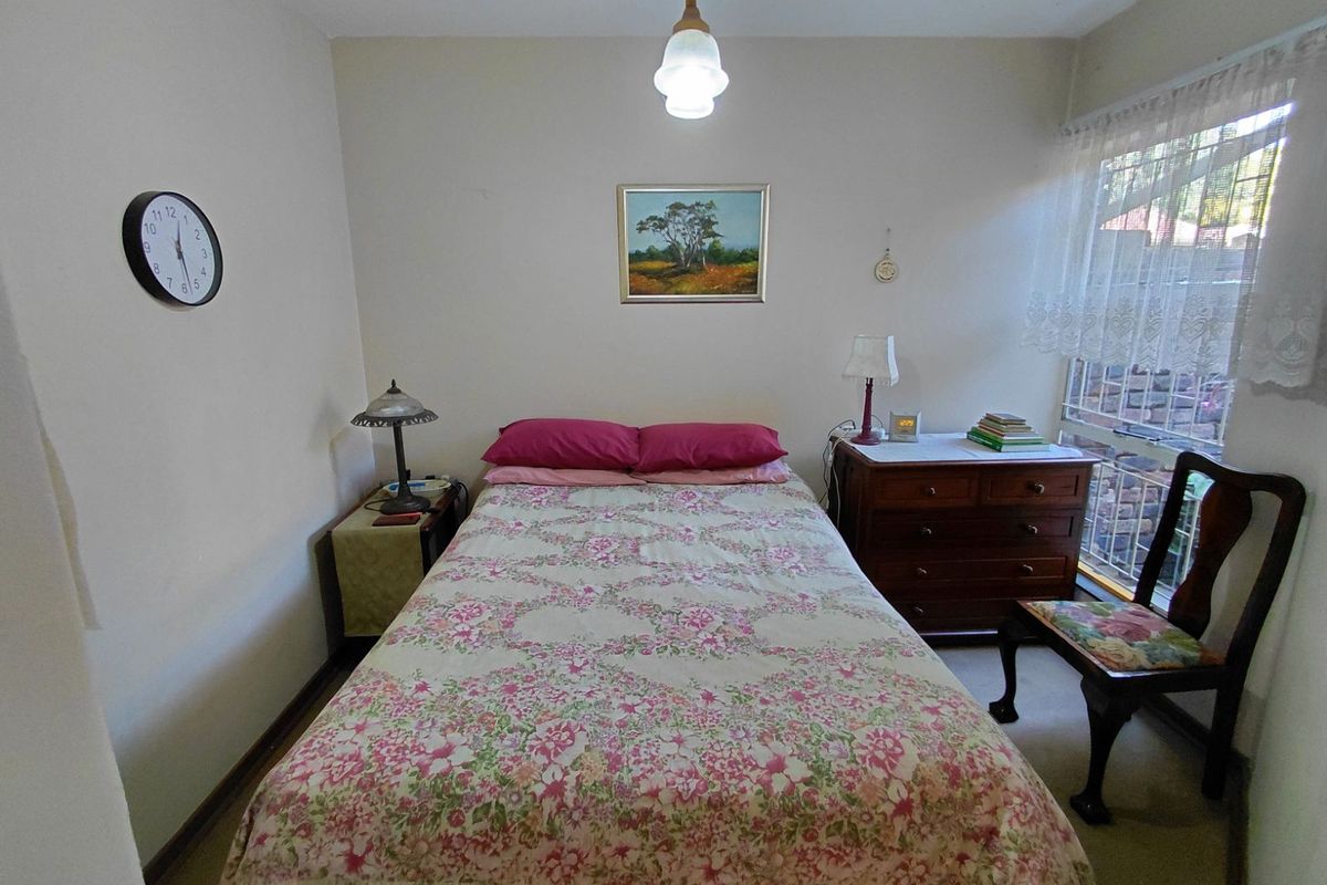A cozy bedroom featuring neutral walls, carpeted flooring, and a large window allowing natural light into the space.