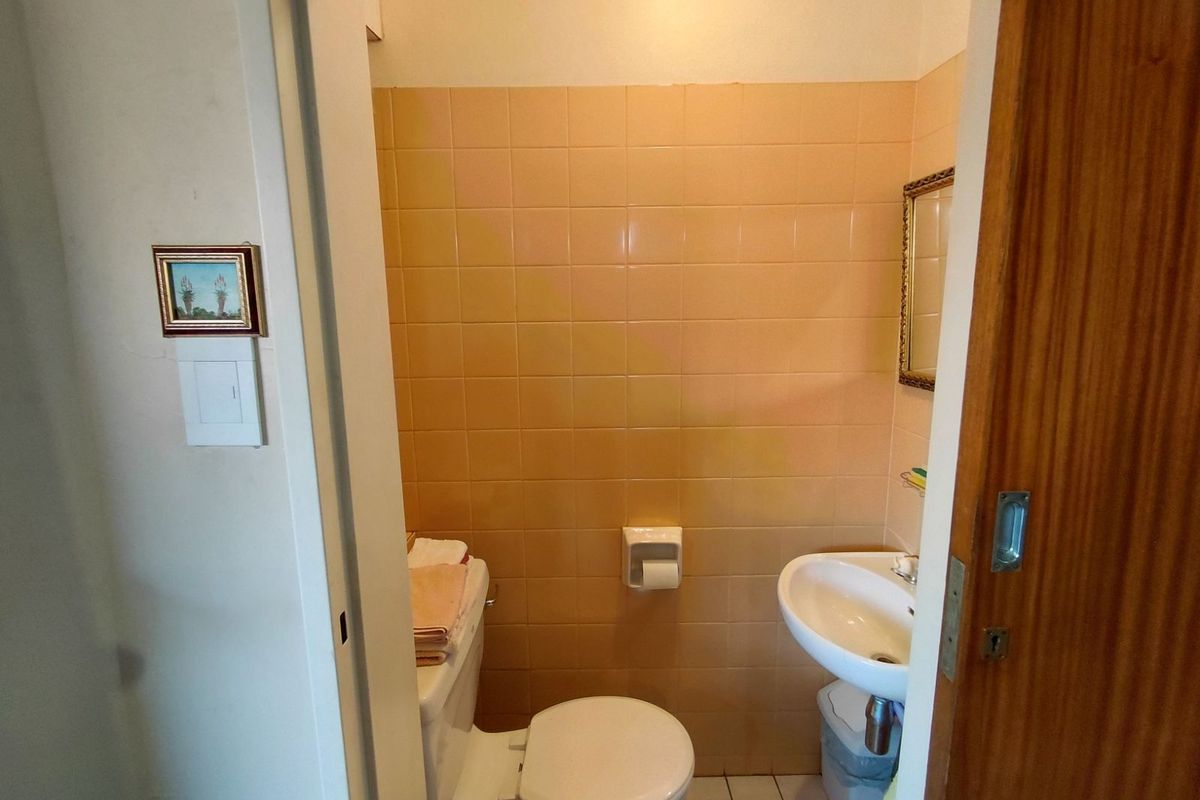 A compact guest bathroom featuring a wall-mounted basin and toilet, finished with dated peach-toned wall tiles.