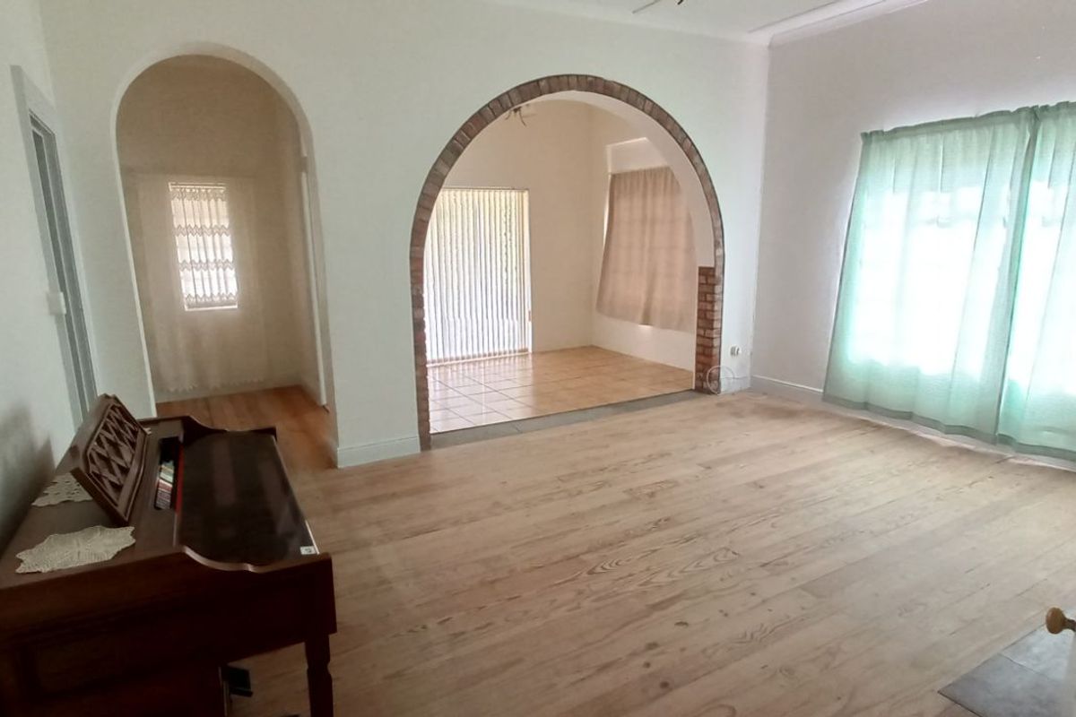 Spacious living area featuring a distinctive brick archway, light wood-look flooring, and large windows allowing for ample natural light.