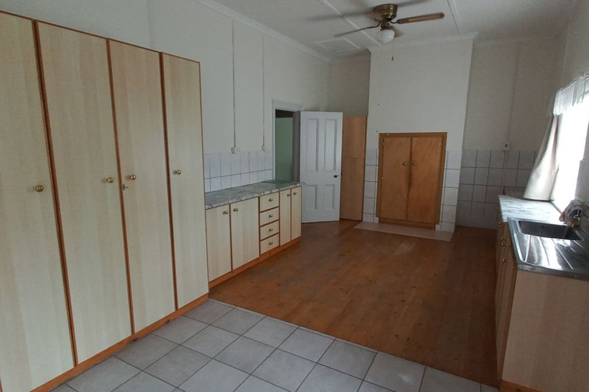 A functional kitchen featuring light wood-look cabinetry, tiled splashbacks, a stainless steel sink, and a combination of tiled and timber flooring.