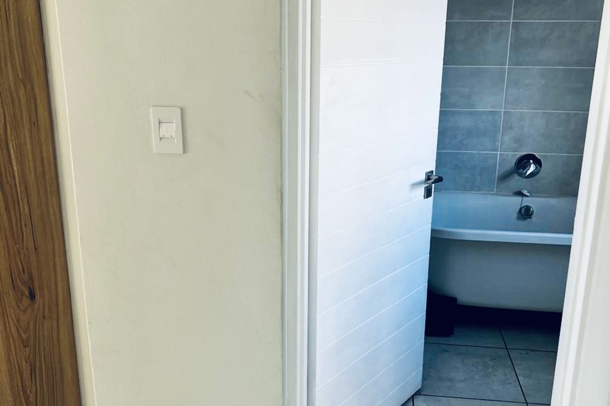 A view through a doorway into a bathroom featuring grey wall tiles, a built-in bathtub, and tiled flooring.