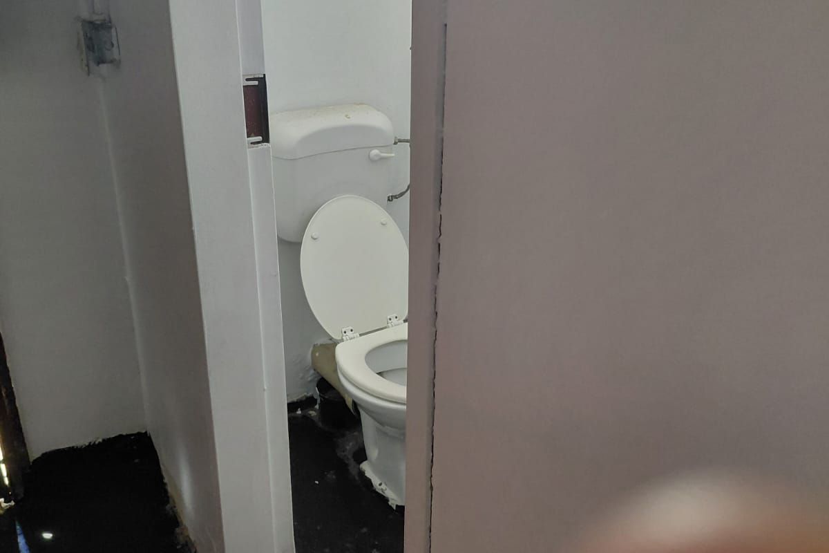 A small, basic restroom facility featuring a standard toilet and dark flooring, requiring maintenance and cosmetic updates.