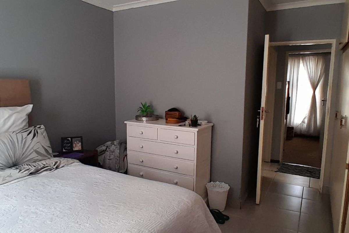 A bedroom featuring built-in cupboards, tiled flooring, and neutral grey wall paint, providing a functional and comfortable living space.