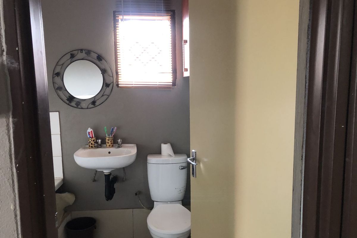 A functional bathroom featuring a wall-mounted basin, a standard toilet, and a window with a wooden blind.