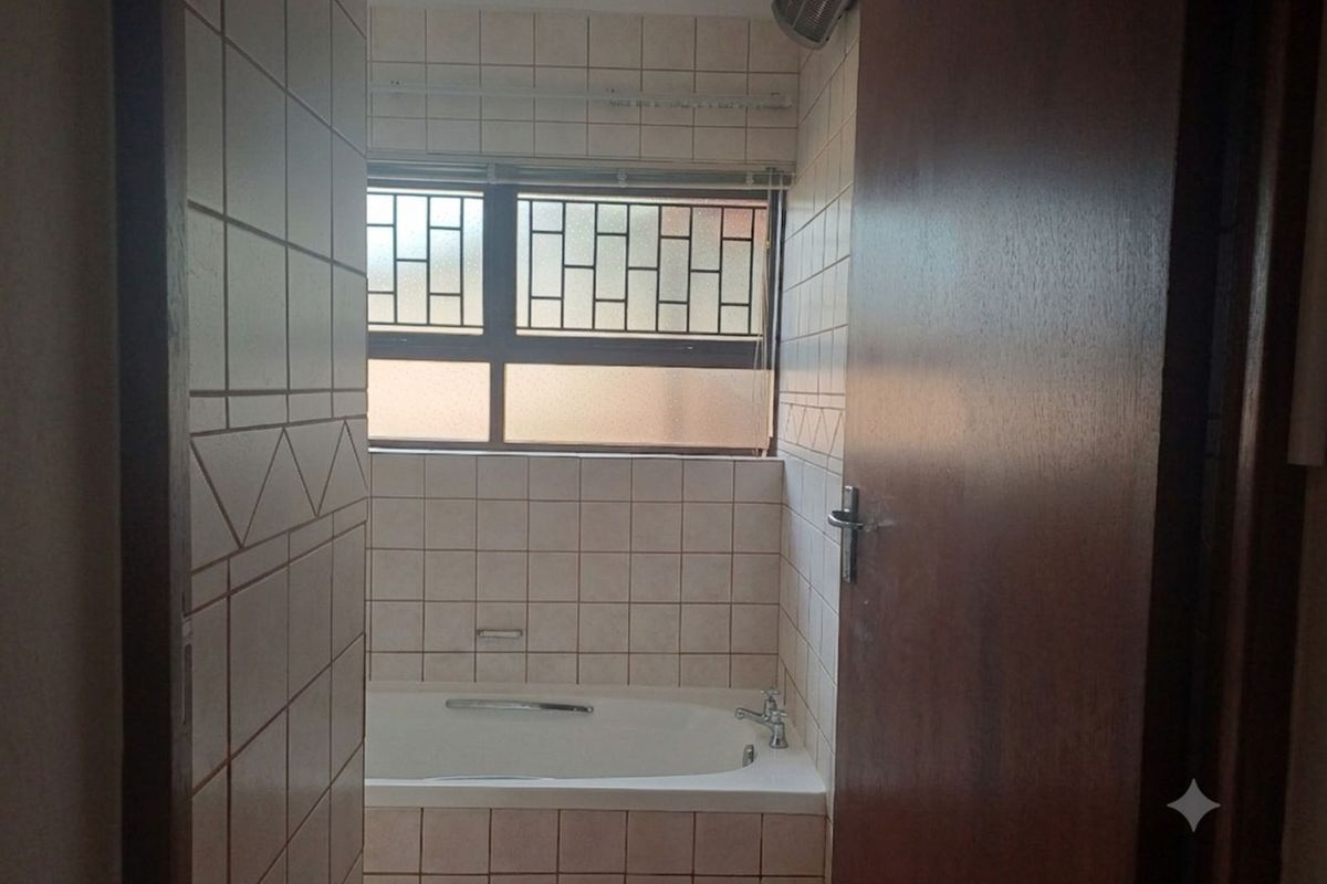 A functional bathroom featuring a built-in bathtub with tiled surround, a window with security bars, and a wooden door.