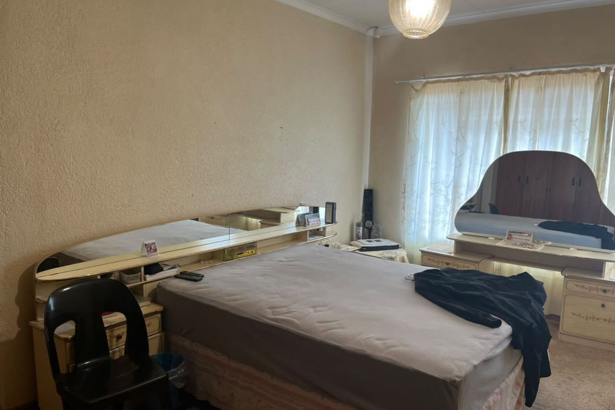A bedroom featuring a built-in headboard unit with integrated mirror and vanity, carpeted flooring, and natural light through window curtains.