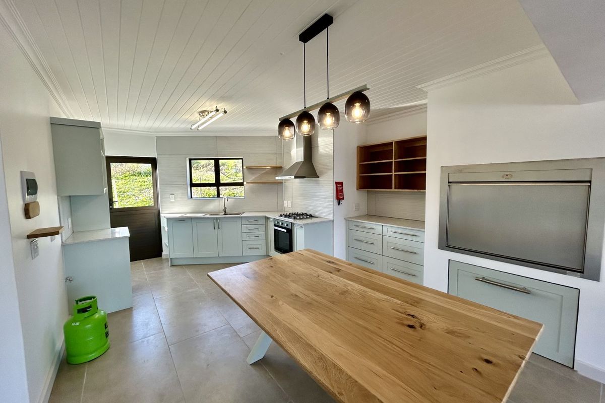 Modern kitchen featuring light cabinetry, built-in oven, gas hob, extractor fan, and a large wooden island, complemented by tiled flooring and tongue-and-groove ceiling.