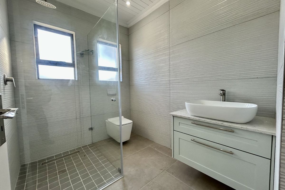 Modern bathroom featuring a walk-in glass shower, wall-mounted toilet, and a contemporary vanity with a vessel sink and stone countertop.