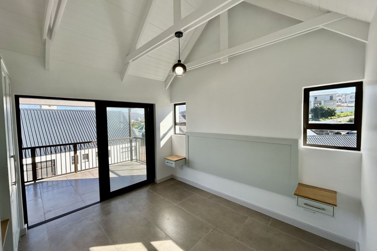 Bright bedroom featuring a vaulted ceiling, tiled flooring, built-in bedside shelving, and sliding glass doors opening onto a private balcony.