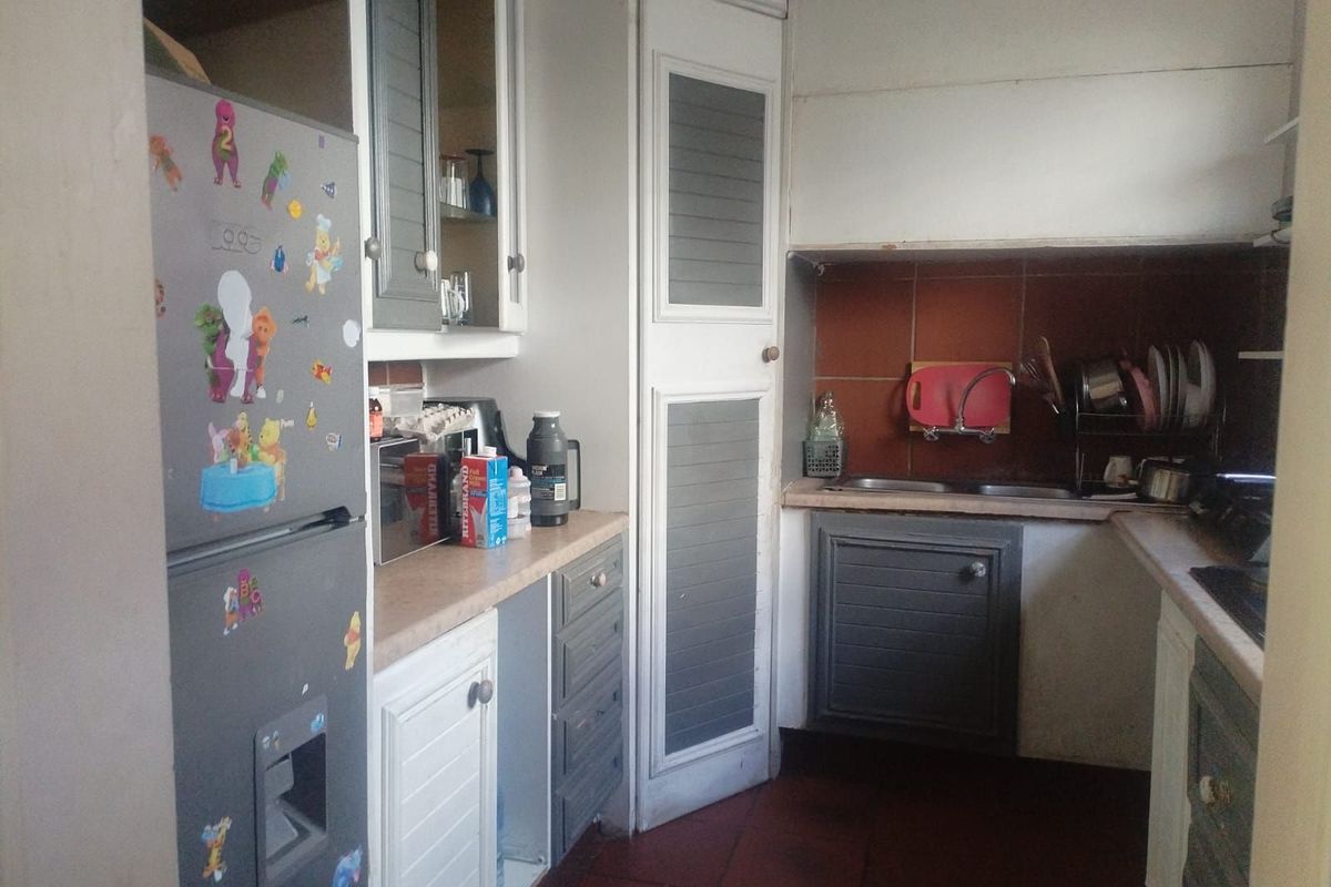 A compact kitchen featuring dated cabinetry, a tiled backsplash, and a double-basin sink, offering a functional layout with potential for modernization.