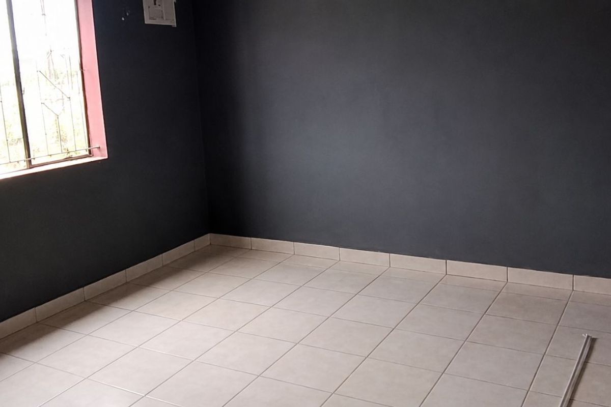 An empty bedroom featuring dark grey painted walls, light-colored floor tiles, and a window fitted with security bars.