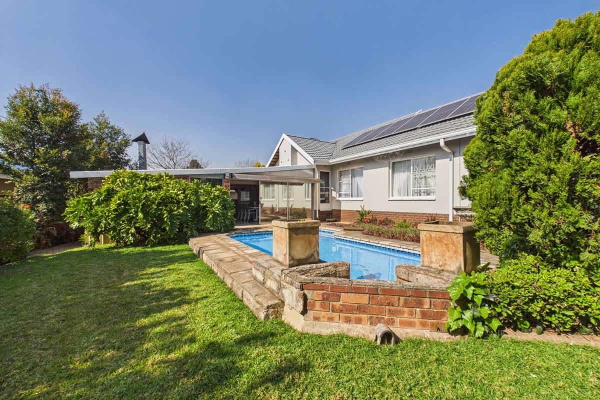 Rear garden featuring a swimming pool with brick surround, covered patio area, and solar panels installed on the tiled roof.