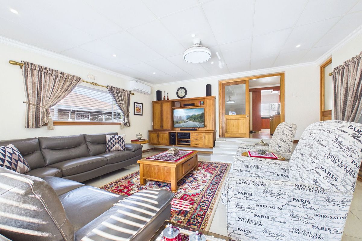 A spacious living room featuring built-in wooden cabinetry, a split-system air conditioner, and tiled flooring, with an adjacent room accessible via a wooden door.