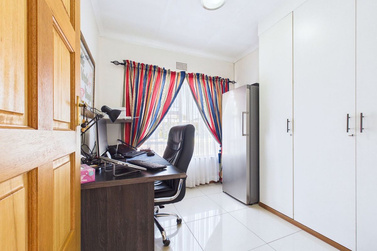 A functional bedroom featuring built-in white cabinetry, tiled flooring, and a window with natural light, currently utilized as a home office space.