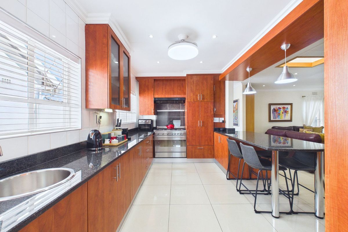 A well-maintained kitchen featuring warm wood cabinetry, granite countertops, a stainless steel gas stove, and an integrated breakfast bar overlooking the living area.