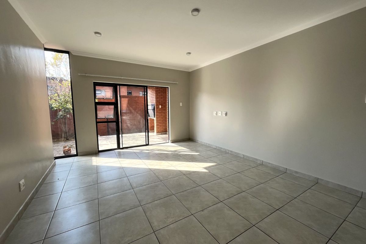 A bright, open-plan living area featuring neutral tiled flooring, recessed ceiling lighting, and large sliding glass doors providing direct access to a private patio.