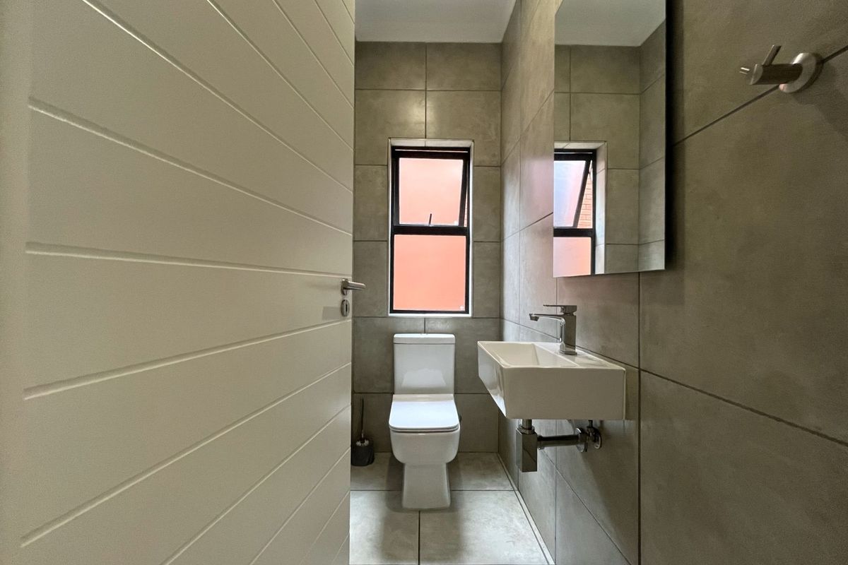 A modern guest cloakroom featuring neutral floor-to-ceiling tiling, a wall-mounted basin, and a sleek toilet.