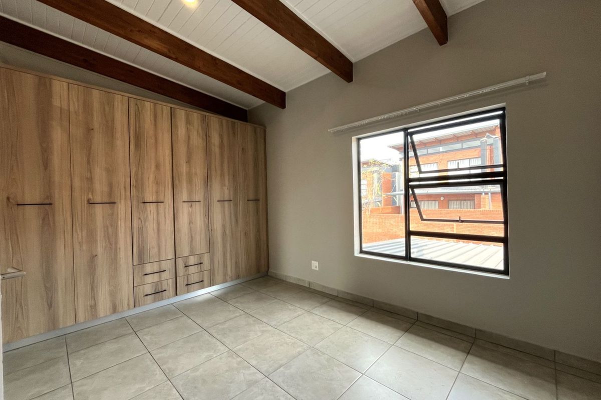 A bright bedroom featuring built-in wooden cabinetry, tiled flooring, and exposed timber ceiling beams, offering a clean and modern aesthetic.