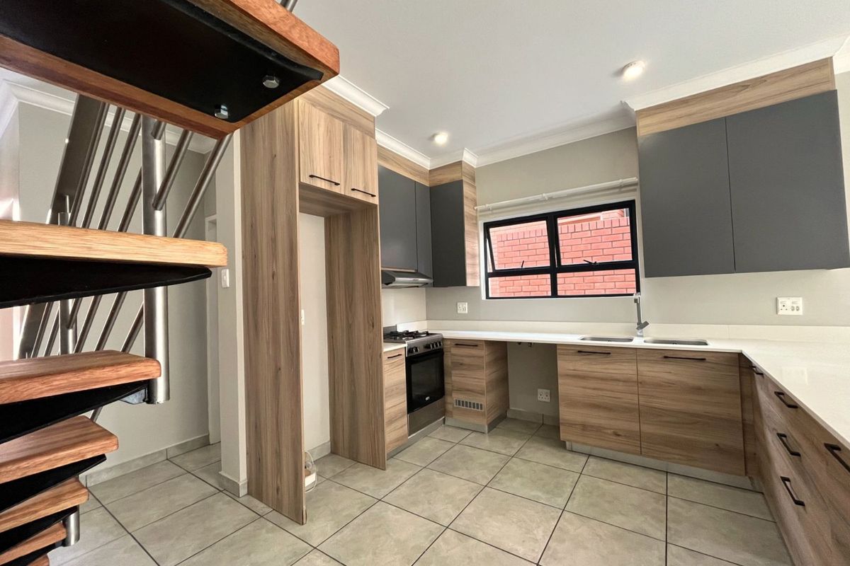 Modern kitchen featuring two-tone cabinetry, stone countertops, integrated stove and extractor fan, tiled flooring, and adjacent spiral staircase.