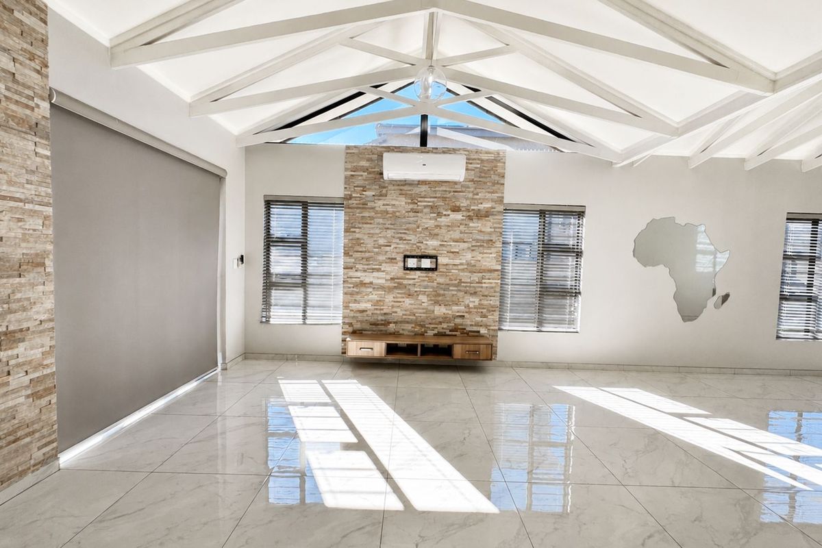 Spacious living area featuring high vaulted ceilings with exposed beams, polished marble-look floor tiles, and a striking natural stone feature wall.