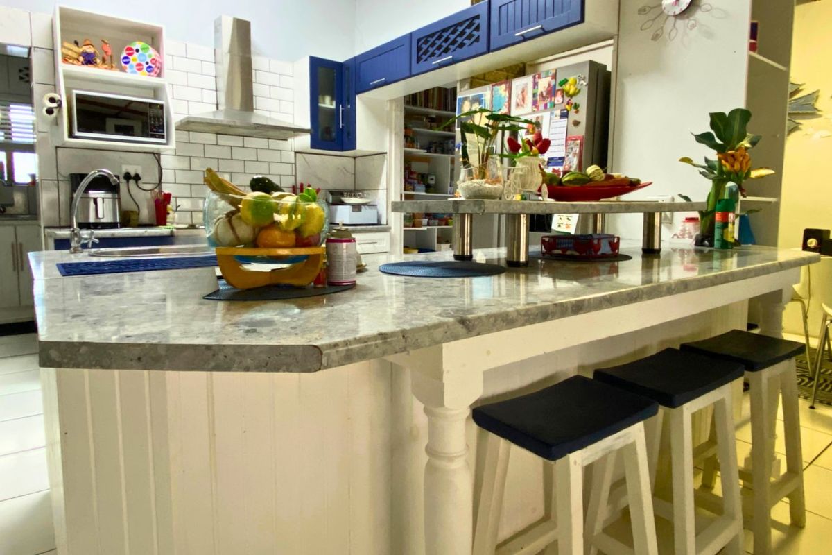 A functional kitchen featuring a central island with stone countertop, subway tile backsplash, stainless steel extractor fan, and blue upper cabinetry.