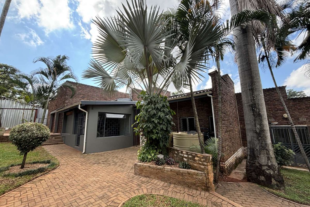 Rear exterior view of the property featuring brick facade, paved courtyard, established palm trees, and a water storage tank.