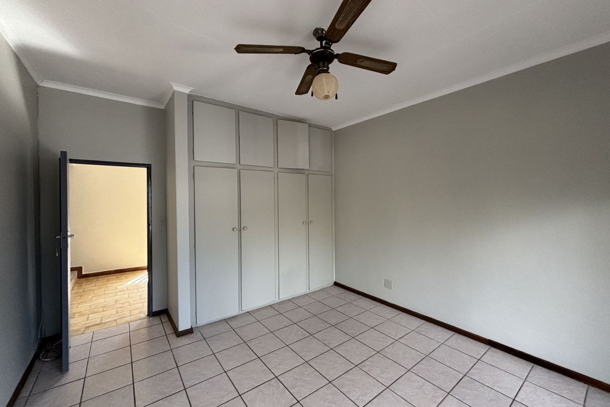 A clean, empty bedroom featuring neutral tiled flooring, built-in floor-to-ceiling cabinetry, and a ceiling fan.