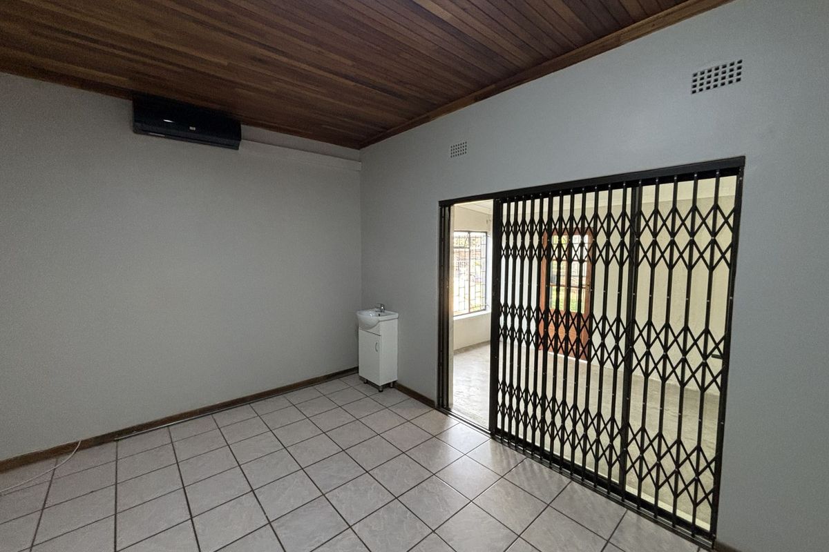 A functional room featuring tiled flooring, a timber-paneled ceiling, a wall-mounted air conditioning unit, and a secure metal sliding gate leading to an adjacent space.
