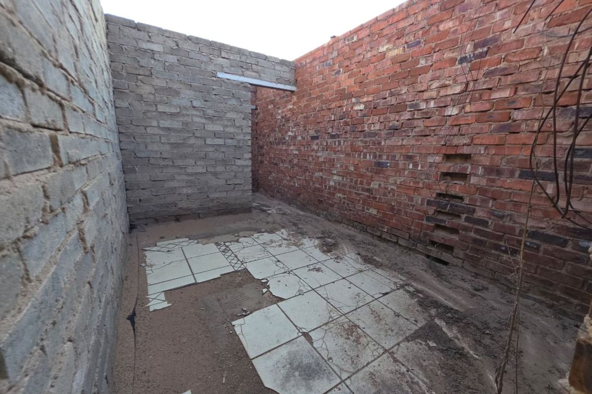 An unfinished outdoor area or courtyard featuring exposed brick walls and damaged tiled flooring, requiring significant renovation and completion.