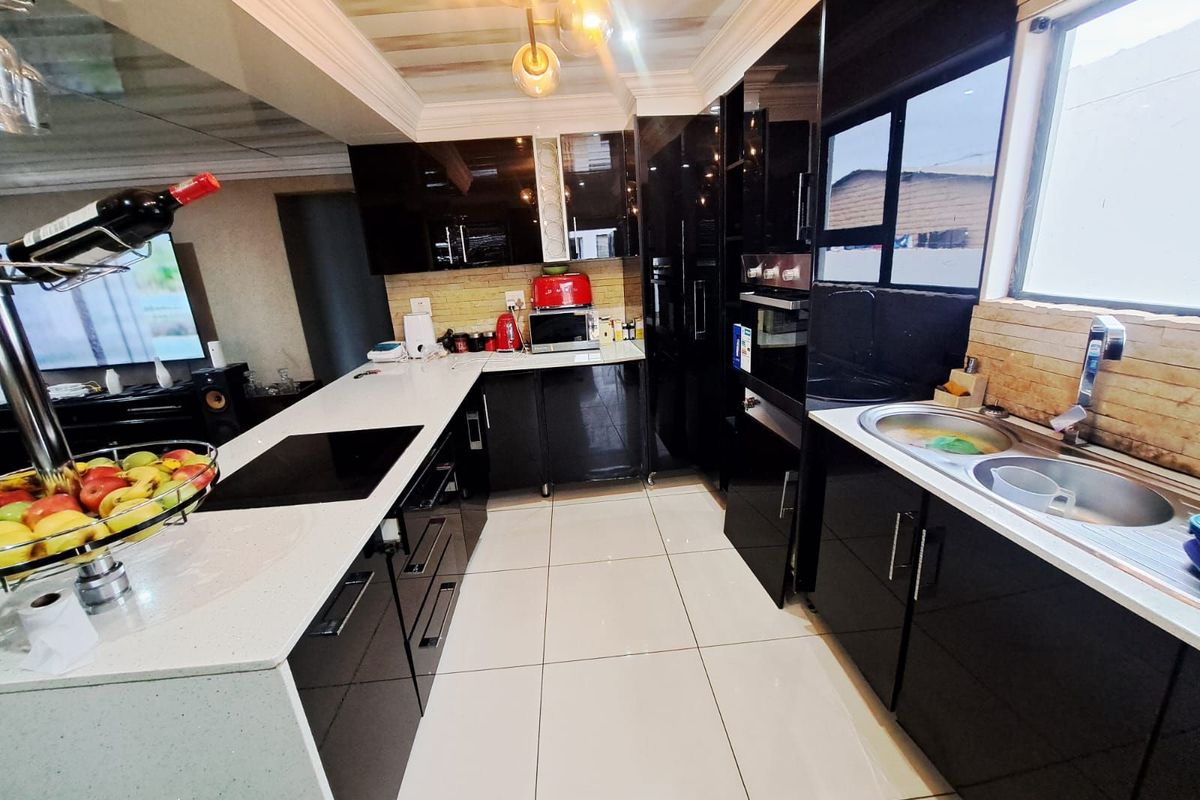 Modern kitchen featuring high-gloss black cabinetry, white stone countertops, integrated oven, and a breakfast bar island with a built-in induction hob.