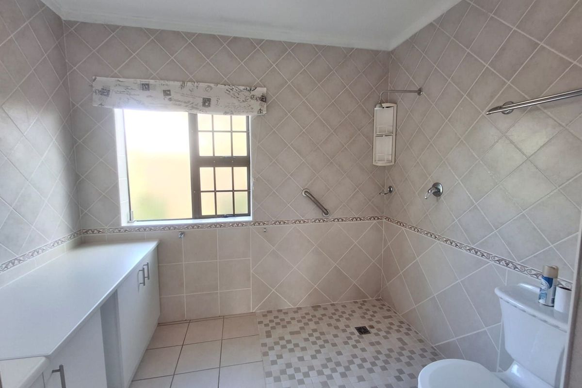 A functional bathroom featuring a walk-in shower area, built-in vanity cabinetry, and neutral wall tiling.