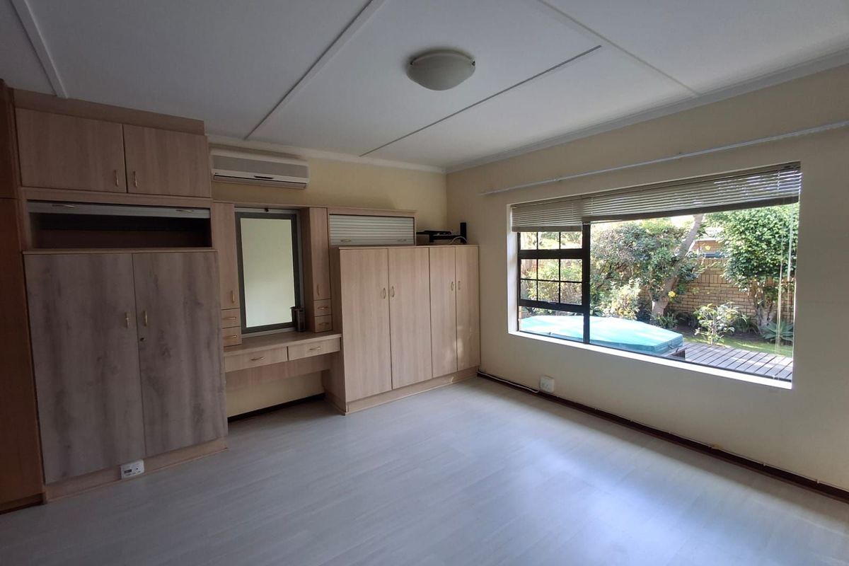 A bedroom featuring built-in wooden cabinetry, a vanity area, and a large window overlooking the garden.
